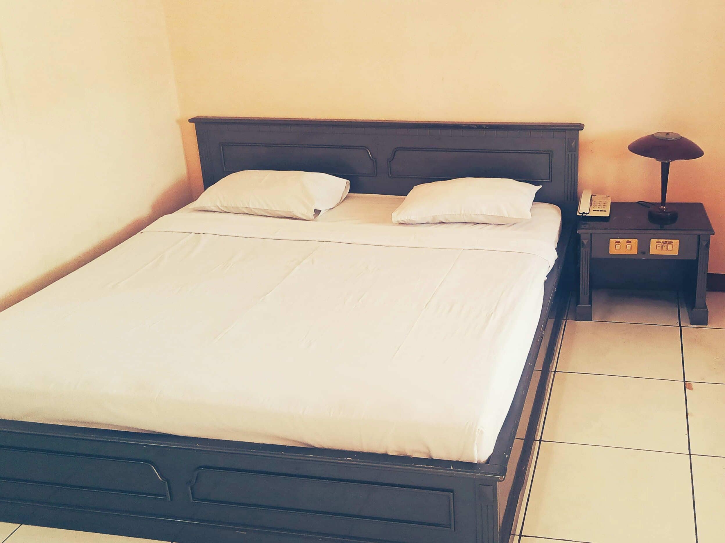 Ein ordentlich gemachtes Bett mit zwei Kissen, ein Nachttisch mit Lampe und Telefon.