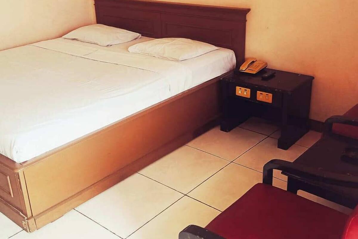 A single bed with a wooden headboard, a bedside table with a telephone, and a chair.
