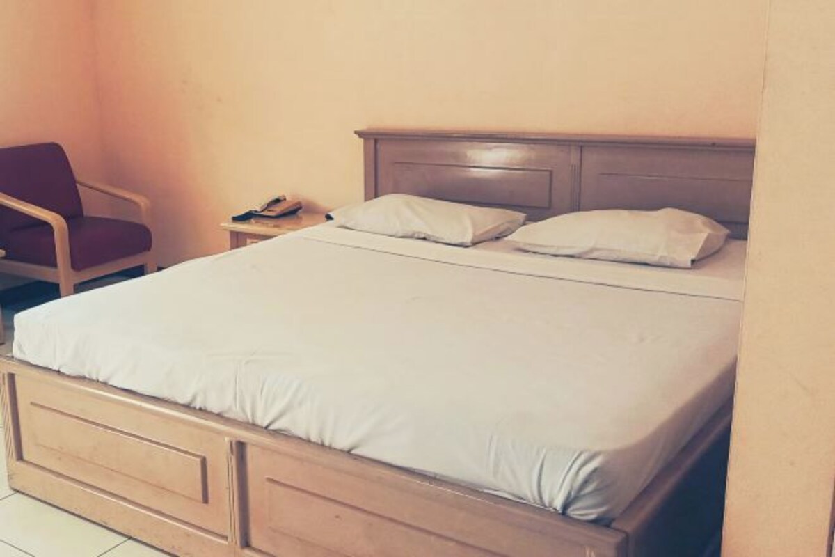 Una cama individual con cabecera de madera, una mesita de noche con lámpara y una silla.