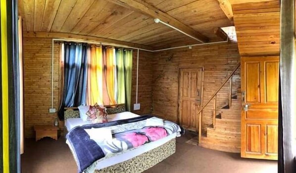 A wooden cabin bedroom with a bed, curtains, a wooden wardrobe, and a staircase.