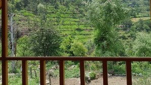 Une vue depuis un balcon en bois donnant sur des champs en terrasses et une colline boisée.