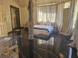 A room with a bed, wooden walls, a large tree trunk, and a mirror.
