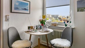 Un'area pranzo con un tavolo apparecchiato per due persone, un quadro appeso al muro e una finestra con vista sugli edifici.