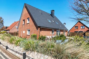 Een bakstenen huis met schuine dak en een satellietschotel, met een tuin vol hoge grassen.