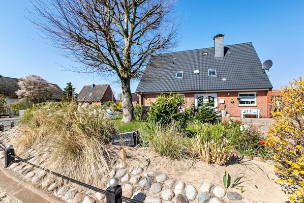 Een woonhuis met een bakstenen gevel, een donker dak en een tuin met verschillende planten en een boom.