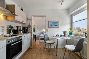 Une cuisine moderne dotée d’appareils électroménagers intégrés, un coin repas avec une table ronde et deux chaises, et une vue sur la ville grâce à une grande fenêtre.