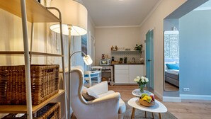 A cozy living room with a sofa, a table with fruit, wicker baskets, a lamp, and a kitchen in the background. - Studio Apartment 'Villa Gute Zeit - Cosy  Apart' with Shared Terrace, Shared Garden and Wi-Fi (Nortorf)