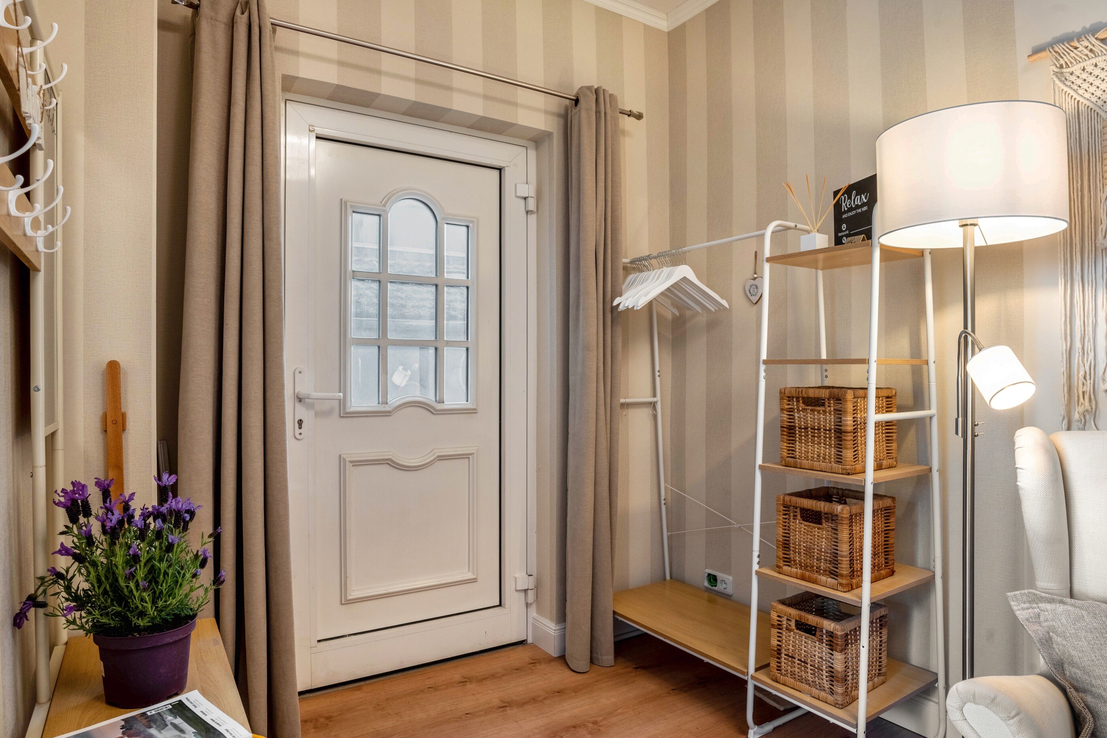 A room with a door, a potted plant, a shelf with baskets, a lamp, and a chair.