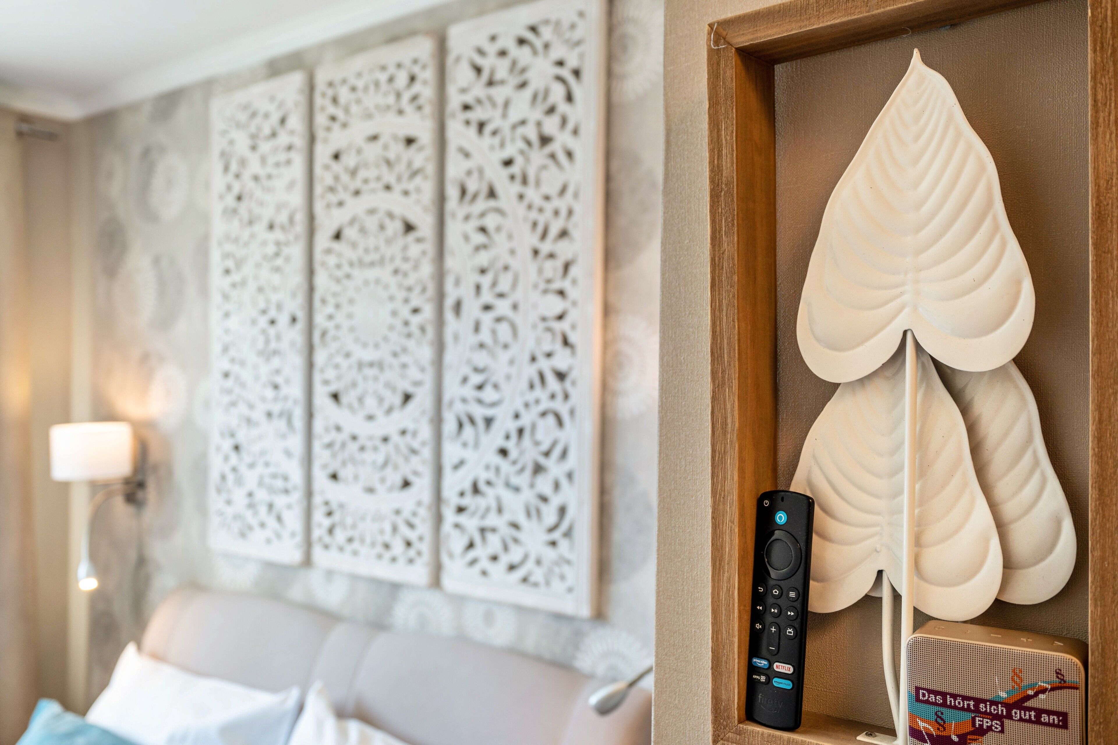 Une chambre moderne avec un canapé, un panneau mural décoratif, une télécommande et un objet décoratif en forme de feuille.