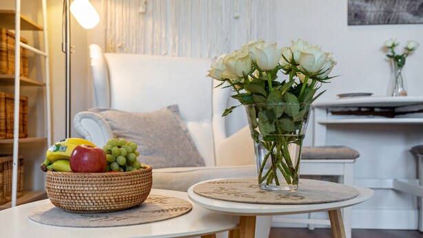 A room with a white sofa, a round table with a woven basket of fruit and a vase of white roses. - Studio Apartment 'Villa Gute Zeit - Cosy  Apart' with Shared Terrace, Shared Garden and Wi-Fi (Nortorf)