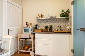 Una cocina compacta con microondas, tostadora y un carrito pequeño con cestas.