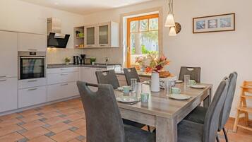 A modern kitchen with white cabinets, a built-in oven, and a dining area with a wooden table and grey chairs.