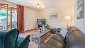 A living room with a sofa, a coffee table, a TV, and a lamp. - Wassermann Vacation Rental with a Terrace, Sauna, and a View of the Achterwasser - (Loddin)