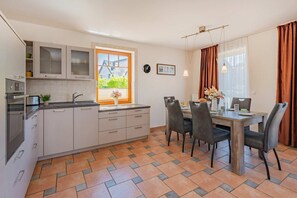 A modern kitchen with a dining area, featuring a window with a view, a clock on the wall, and a dining table with chairs.