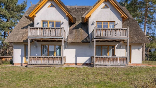 A two-story house with a thatched roof, wooden balconies, and a white exterior. - Wassermann Vacation Rental with a Terrace, Sauna, and a View of the Achterwasser - (Loddin)