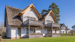 A two-story chalet with a thatched roof, wooden balconies, and a well-maintained lawn. - Wassermann Vacation Rental with a Terrace, Sauna, and a View of the Achterwasser - (Loddin)