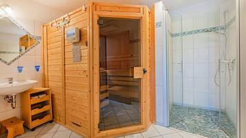 Eine Sauna mit Holzaußenverkleidung, einer Glastür, einem Waschbecken und einem Duschbereich mit gefliesten Wänden.