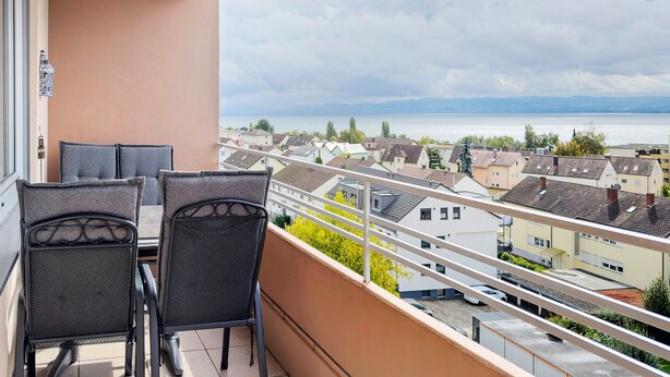 A balcony with two chairs, a view of a lake, and buildings in the background. - Holiday Apartment 'Bodenseewohnung Bär' with Lake View, Balcony, and Wi-Fi (Immenstaad am Bodensee)