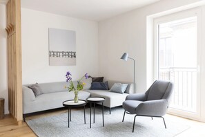 A modern living room with a grey sofa, a grey armchair, two round tables, and a floor lamp.