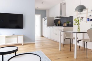 A modern kitchen with white cabinets, a black TV, and a dining area with a table and chairs.