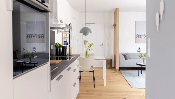 A modern kitchen with white cabinets, a dining area with a white table and chairs, and a living room with a sofa and a coffee table. - Apartment 'Steuerbord' with Balcony and Wi-Fi (Sankt Peter-Ording)