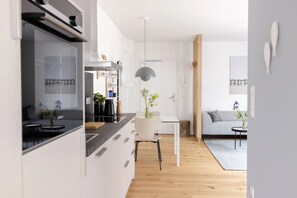 Une cuisine moderne avec des meubles blancs, un coin repas avec une table et des chaises blanches, et un salon avec un canapé et une table basse.