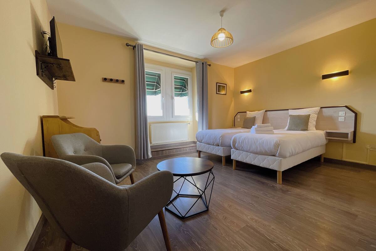 Quarto de hotel com duas camas, um sofá, uma mesinha e uma janela com cortinas.