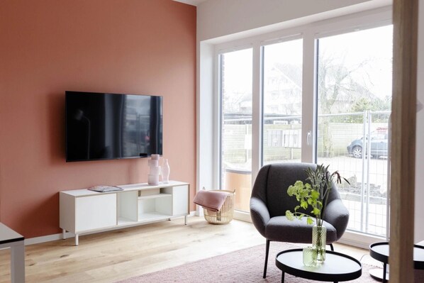 Un salon moderne avec un téléviseur à écran plat, un fauteuil gris, une console blanche et une grande fenêtre.