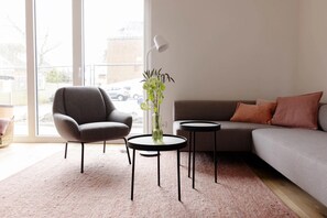 Un salon moderne avec un canapé gris, un fauteuil gris et une petite table ronde sur laquelle est posé un vase de fleurs.