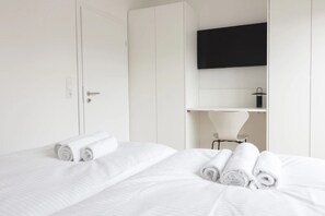 Une chambre d’hôtel avec un lit, un téléviseur fixé au mur et une petite table avec une lampe.