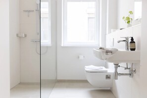 Une salle de bain moderne avec une douche à parois de verre, des toilettes blanches et un lavabo surmonté d’un miroir.