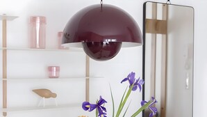 A white table with a clear glass vase containing purple and orange flowers, a dark pendant light, and a mirror on the wall.