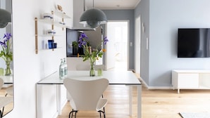 A modern kitchen with white cabinets, a dining table with chairs, and a large TV on the wall. - Apartment 'Backbord' with Balcony and Wi-Fi (Sankt Peter-Ording)