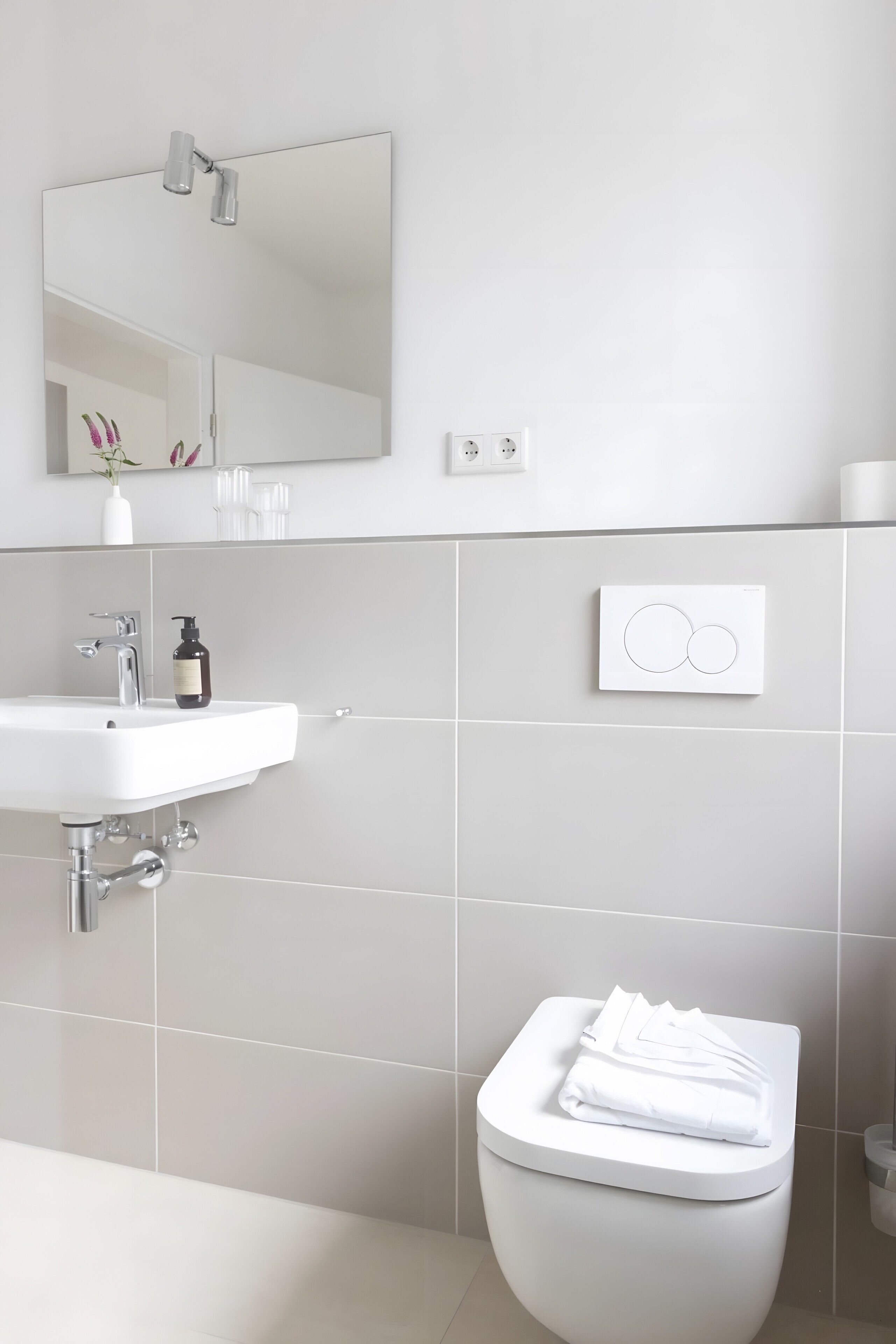 A modern bathroom with a white sink, mirror, and toilet.