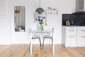 Een moderne keuken met witte kasten, een eettafel met twee stoelen, een hanglamp en een spiegel aan de muur.