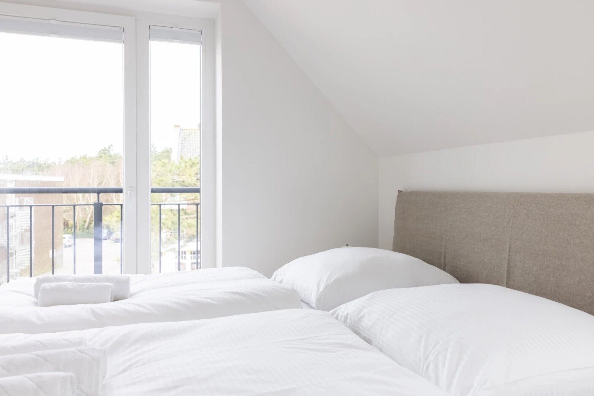 A hotel room with two beds, a balcony, and a view of the outside.