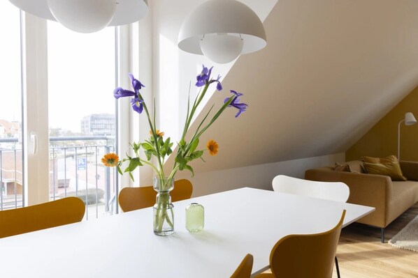Un coin repas avec une table blanche, des chaises jaunes et un vase rempli de fleurs.