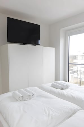 Une chambre d’hôtel avec deux lits, un téléviseur à écran plat fixé au-dessus des lits et une grande fenêtre donnant sur la ville.
