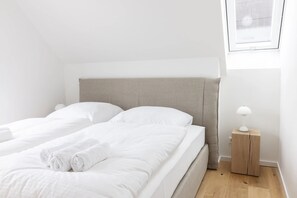 Un lit bien fait, avec du linge de lit et des serviettes blanches, une table de chevet avec une lampe et une fenêtre donnant sur un beau paysage.