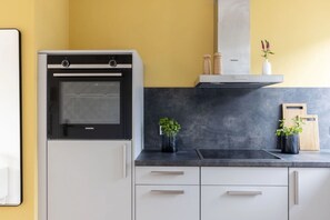 Une cuisine équipée d’un four Siemens, d’un plan de travail noir, de meubles blancs et d’un mur jaune.