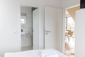 Quarto com cama, banheiro com pia e toalha, e varanda com cadeiras.