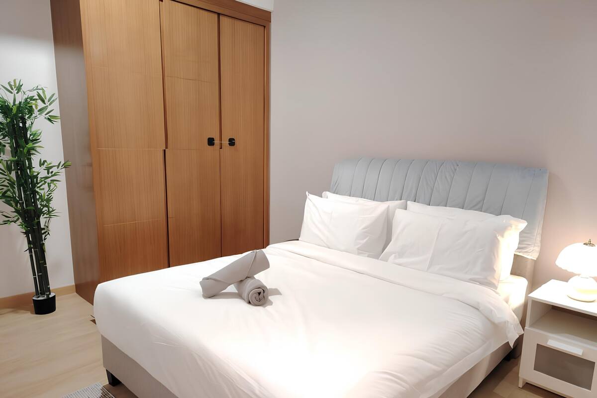 A neatly made bed with white linens, a headboard, and a bedside table with a lamp.