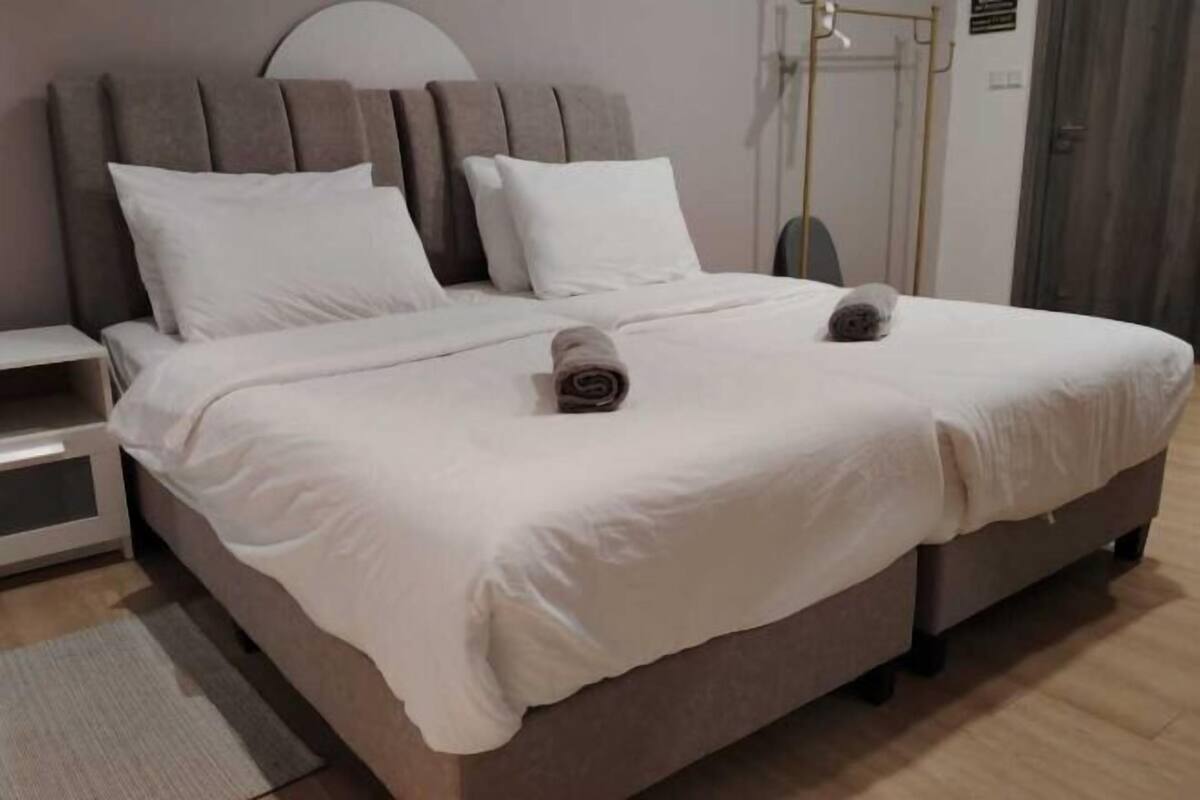 A neatly made bed with white linens and two rolled towels, a bedside table, and a wall-mounted light fixture.