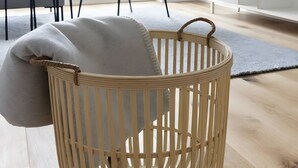 Un salon moderne avec un panier en osier, un fauteuil gris et un téléviseur à écran plat fixé au mur.