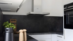 Une cuisine moderne avec des meubles blancs, un plan de travail noir, un four en acier inoxydable et une hotte aspirante noire.