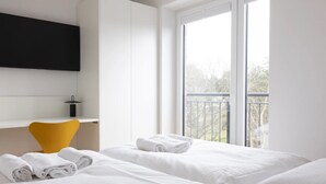 Une chambre d’hôtel avec deux lits, un bureau, une chaise et une grande fenêtre donnant sur un balcon.