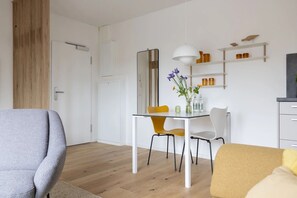 Een moderne woonkamer met een bank, een eettafel met stoelen, een spiegel en een plank met decoratieve objecten.