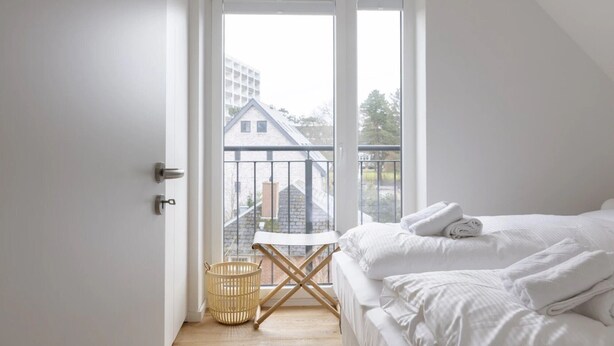 Une chambre à coucher avec un lit, une petite table, un panier en osier et un balcon doté d’une balustrade.