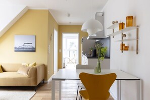 A modern interior with a dining area, a sofa, and a kitchen visible through an open door.