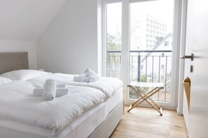 A modern bedroom with a large bed, a small table, and a balcony with a view of buildings.